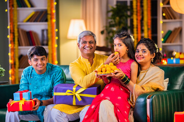 Indian family enjoying Diwali festival night with sweets and gifts in traditional attire at home