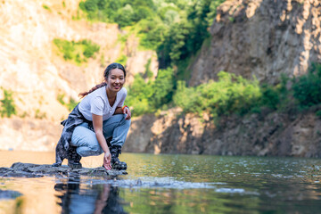 a young woman squats by the shore of the lake and enjoys the refreshing coolness and beauty of the lake