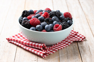 Fresh assortment berries in bowl on wooden table.