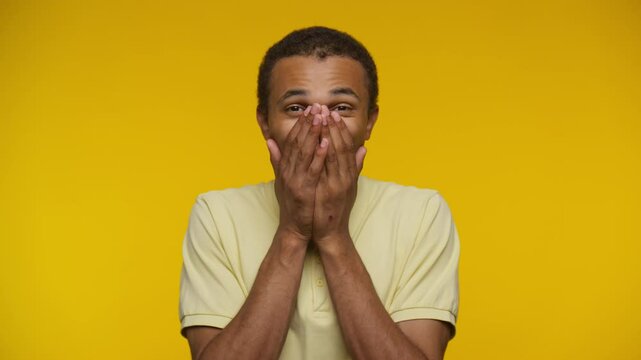 Surprised young man covering his mouth with hands on a yellow background