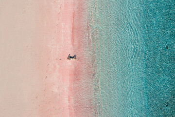 Top view of a girl sitting on the pink sand beach and blue sea in Komodo, Indonesia © Patrick.W
