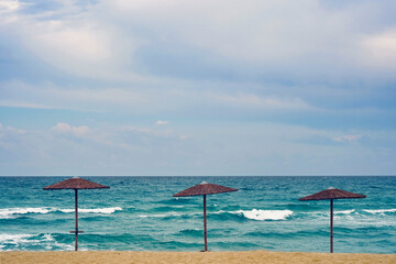 Еmpty beach with sand, see, sky and three strawy umbrellas in decreasing height, suitable for chart graphically reflecting a decreasing or increasing trend