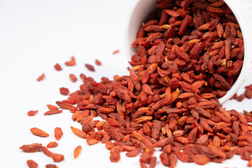 Dried goji berries spilled out of a plate on a white background.