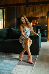 Woman in floral dress sitting on sofa and looking at heel of her new pink stilettos