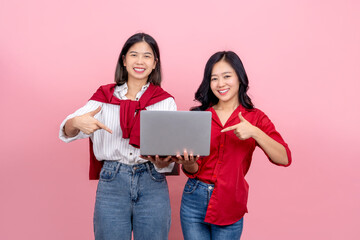 Two beautiful Asian girls use laptops on pink background.