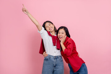 Happy loving lesbian couple good time together with finger pointing to copy space isolated on pink background.