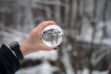 Naklejka premium Hand holding a glass ball, trees with snow reflected in it