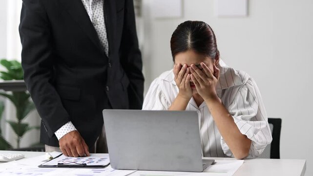 Stressed businesswoman reacts to supervisor's criticism in office. Struggling, she buries her face in hands, showing signs of pressure and frustration.