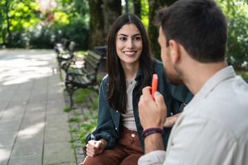 Young man and woman sitting in the park giving interview for media about life standard and travel....