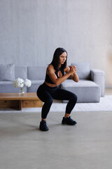 Young fit woman in sportswear do squat exercise indoors in living room. Online indoors workout. Training at home