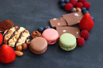 Macarons, chocolate, cookies, berries and various nuts on dark blue background. Selective focus.