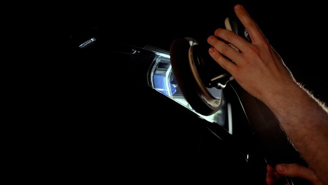 Skilled car mechanic polishing a headlight with an electric buffer in an auto repair shop, focusing on top-notch service and maintenance for vehicles. Intricate work captured in close-up view.