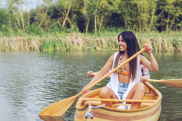 Woman rowing a canoe in a serene natural setting, smiling.