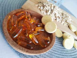 Fish oil capsules with omega 3 and vitamin D3 in wooden bowl