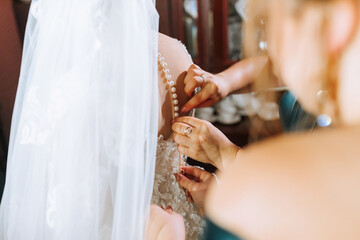 A bride is getting ready for her wedding and her bridesmaids are helping her. The bride is wearing...
