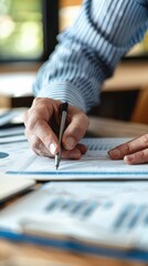 Close-up of a person's hand writing with a pen on paperwork, focused on business charts and financial documents on a desk.