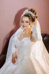 A woman in a wedding dress is posing for a picture. She is wearing a tiara and has her hand on her...