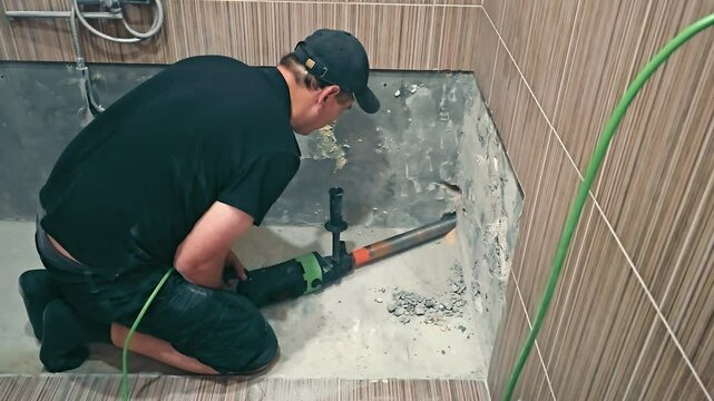 Worker Drilling in a Bathroom Renovation, A construction worker in a black shirt and cap is using a power drill to renovate a bathroom