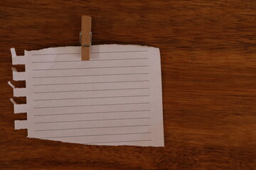 Blank sheet of paper with lines, torn with clothespin hanger, dark brown wood background.