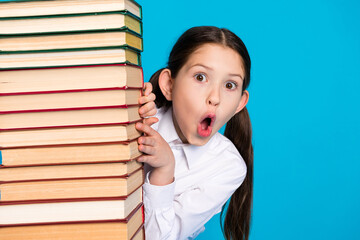 Portrait of little schoolchild peek pile stack book wear uniform isolated on blue color background