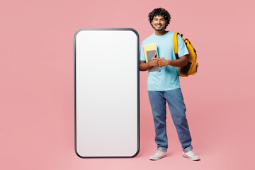 Full body young Indian boy student wear blue casual clothes backpack bag hold books big huge blank screen mobile cell phone isolated on plain pink background. High school university college concept.