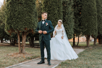 A man and a woman are standing in a park, the man is wearing a suit and tie