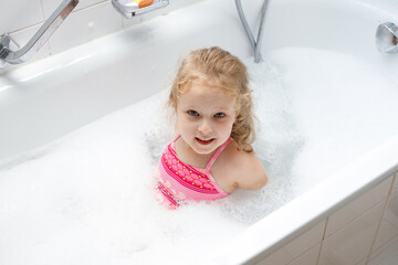 Cute little girl taking bubble bath at home