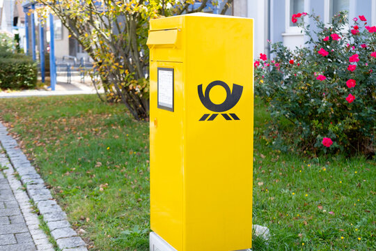 German Yellow Deutsche Post mailbox standing in park with flowers and greenery around, symbolizing postal services in Germany, Frankfurt - May 28, 2024