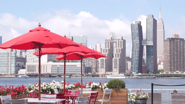New York City waterfront skyline, Manhattan Midtown buildings, riverfront skyscrapers, cafe umbrellas by East river water. Waterside cityscape from Hunters Point, Long Island, Queens, United States.