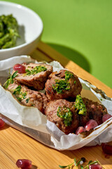 healthy pork kebab served on a wooden board. The kebab is wrapped in parchment paper and garnished with fresh herbs, served with a side of vibrant green pesto.