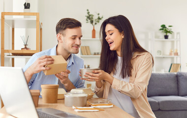 Happy married couple sits at a table in their home, eating a takeaway meal or delivery food. Their lunch is filled with joy and contentment, highlighting the happiness of dining together.