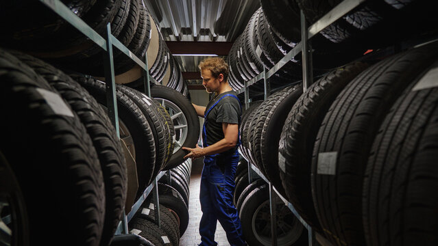 Hardworking experienced worker holding tire and he wants to change it In the tire store. Selective focus on tire.