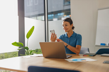 A focused professional woman interacts with her smartphone at a sleek office desk, enhancing productivity.