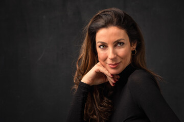 Close-up studio portrait of an attractive woman smiling against isolated dark background