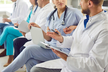 A close-up cropped shot of a group of young professionals, doctors team in scrubs uniform, sitting in a meeting. They are listening to new information and taking notes, discussing work-related issues.