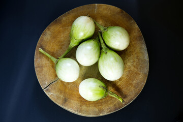 Green eggplant on a wooden cutting board. Top view Thai eggplant on cutting board on black background. Rustic kitchen, vegetable, cooking, and nutrition concepts. Close-up small green eggplants.