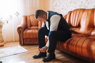 A man in a suit is sitting on a couch, fixing his shoes