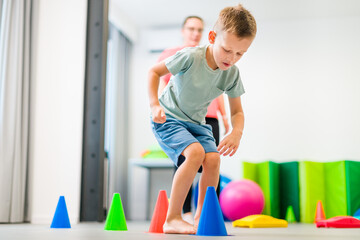 Young boy exercising with female physical therapist during therapy session. Child occupational...