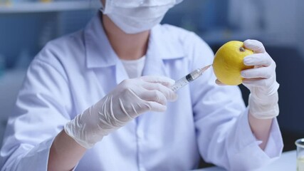 Macro high angle shot video of experiment concept on laboratory background. A scientist with medical gloves uses a medical syringe to inject clear chemical liquid into a fresh lemon in the other hand - Powered by Adobe