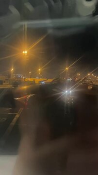 Airport apron controller (ground traffic) with red marshalling light wand, directing a departing plane out of the parking zone at night. Aircrafts parked in the background. Plane departing airport.