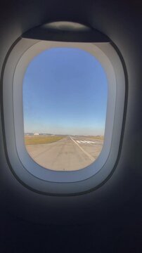 View of airport apron, runway, POV video from passenger porthole window. Plane after landing taxis in airport apron tarmac towards arrival gate for passenger deboarding. Daytime, clear blue sky