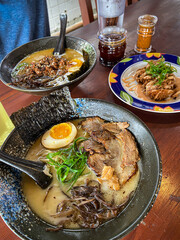 Japanese pork miso ramen consisting of broth, miso, pork, sliced scallions, sliced mushrooms, soft half boiled egg or ajitsuko tamago ajitama in a bowl on a wooden table.