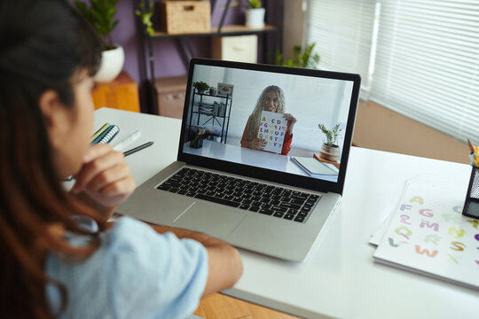 Person participating in virtual learning session observing tutor on laptop screen holding color coded alphabet letters indoors notebook placed on desk