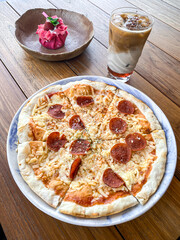 Freshly cooked Italian pizza with various cheese and sausage toppings in ceramic plate on wooden table.