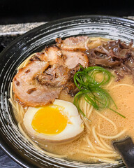 Japanese pork miso ramen consisting of broth, miso, pork, sliced scallions, sliced mushrooms, soft half boiled egg or ajitsuko tamago ajitama in a bowl on a wooden table.