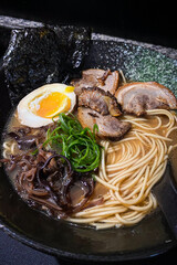 Japanese pork miso ramen consisting of broth, miso, pork, sliced scallions, sliced mushrooms, soft half boiled egg or ajitsuko tamago ajitama in a bowl on a wooden table.