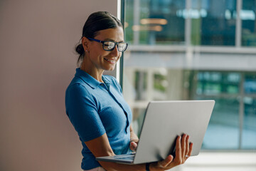 A dedicated and focused woman wearing glasses intently using her laptop within a stylish and modern office space