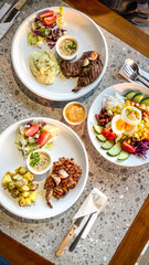 Flat lay photo of beef and chicken steak with garnished fresh vegetable salad and mashed potatoes at a western cuisine restaurant.