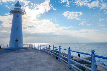 A small white lighthouse stands at the end of a breakwater