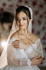 A woman in a wedding dress is posing for a picture. She is wearing a veil and has her arms around her. The image has a warm and romantic mood